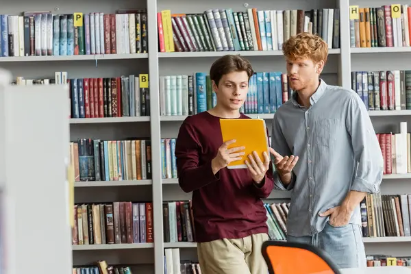 Двоє студентів чоловічої статі занурюються у світ книг на книжковій полиці. — стокове фото