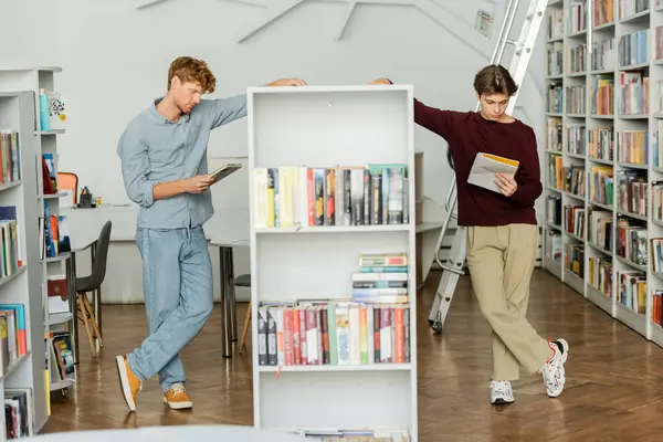 Двое молодых людей, погруженных в учебу посреди библиотеки, полной книг. — стоковое фото