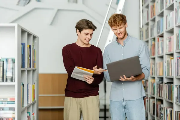 Two men in a library, engrossed in a laptop screen. — Stock Photo
