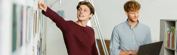Two young men studying together, one standing, one using laptop. — Stock Photo