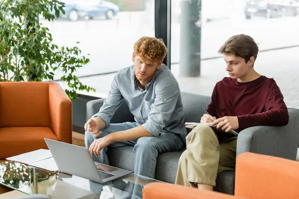Two men engrossed in work, sitting on couches with laptops. — Stock Photo