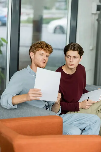 Due studenti maschi profondamente impegnati nello studio delle carte sul divano. — Foto stock