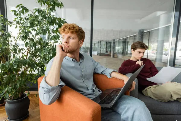 Two young men, one on laptop, studying on a couch. — Stock Photo