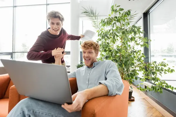 Two male students work together on a laptop while sitting on a couch. — Stock Photo