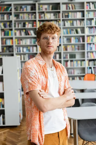 A young man stands, surrounded by countless books in a library. — Stock Photo