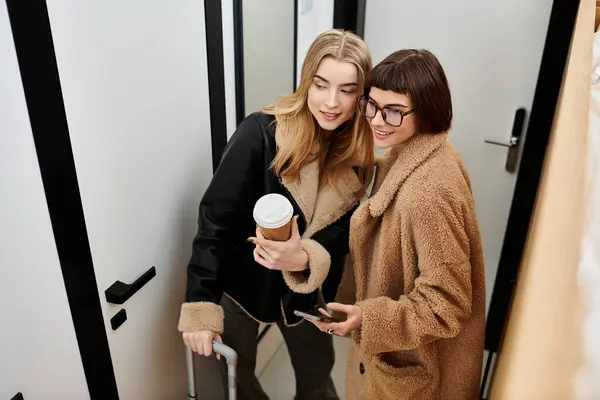 Dos mujeres, una joven pareja lésbica, se paran una al lado de la otra, con equipaje a sus pies - foto de stock