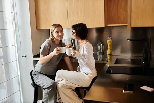 Um jovem casal lésbico desfrutando de café juntos em um balcão de cozinha dentro de um quarto de hotel. — Fotografia de Stock
