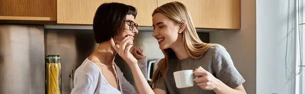 Una giovane coppia lesbica in possesso di tazze di caffè, chiacchierando e in piedi in una cucina elegante di una camera d'albergo. — Foto stock