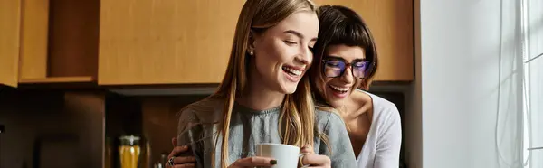 Deux jeunes femmes, un couple de lesbiennes, se tiennent dans une cuisine d'hôtel, partageant un moment confortable et rempli de café ensemble. — Photo de stock