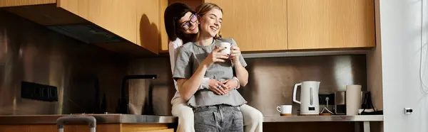 A young lesbian couple stands in a hotel kitchen, enjoying coffee together. — Stock Photo