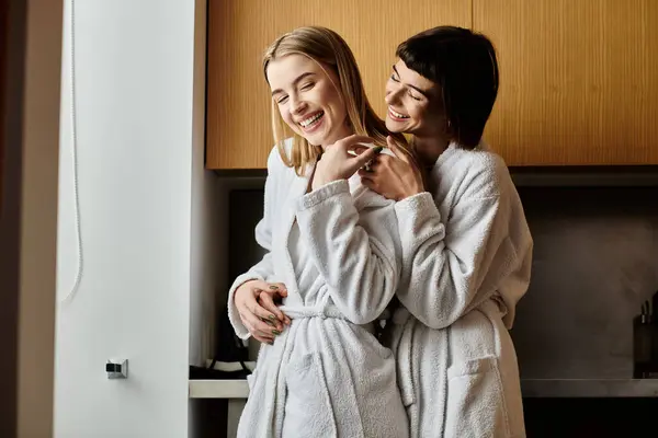 Um jovem casal lésbico se reúne em roupões de banho em um quarto de hotel, exalando tranquilidade e intimidade. — Fotografia de Stock