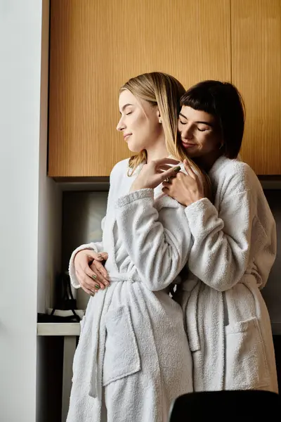 A young lesbian couple in bath robes, standing side by side in a hotel room, exuding serenity and love. — Stock Photo