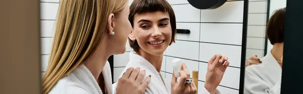 Una joven vestida con una bata de baño se para delante de un espejo, limpiando diligentemente sus dientes. - foto de stock