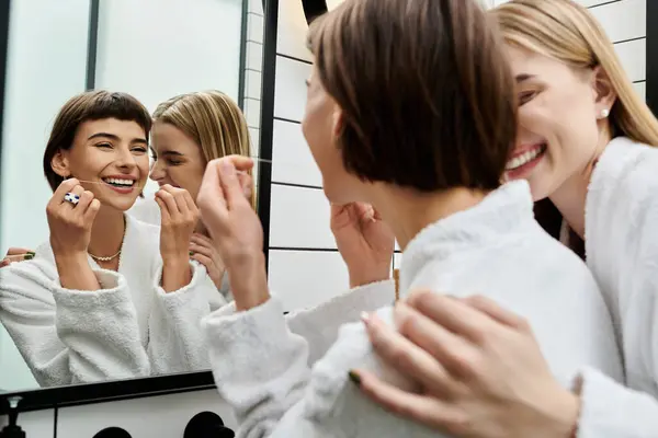 Una joven con una bata de baño lavándose los dientes con cuidado frente a un espejo, encarnando una tranquila rutina matutina. - foto de stock