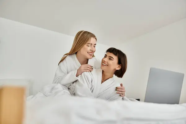 Um jovem casal lésbico de roupões de banho deitado junto na cama, compartilhando um momento terno de conexão e relaxamento. — Fotografia de Stock