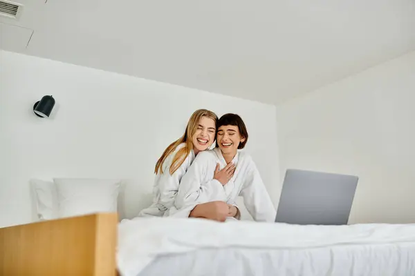 Belo casal lésbico em roupões de banho desfrutando de um momento aconchegante sentado em uma cama de hotel de luxo. — Fotografia de Stock