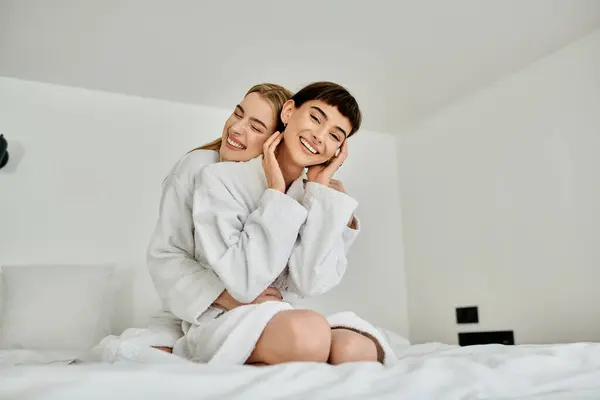 Un beau couple de lesbiennes en peignoirs de bain s'assoit paisiblement sur un lit confortable à l'intérieur d'une chambre d'hôtel. — Photo de stock