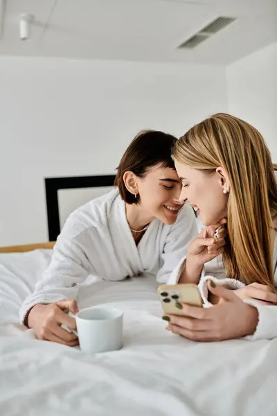 Deux femmes en peignoirs de bain reposent paisiblement côte à côte sur un lit d'hôtel luxueux, partageant un moment tendre de proximité et de connexion. — Photo de stock