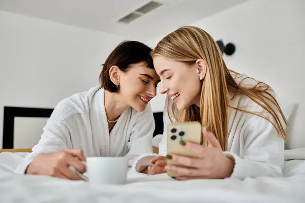 A beautiful lesbian couple in bath robes, peacefully laying next to each other on a cozy bed in a hotel room. — Stock Photo