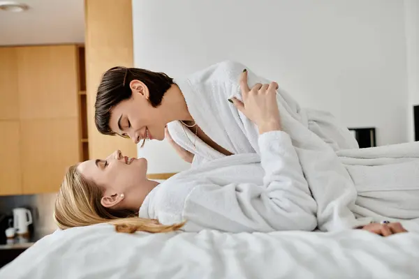 Casal em roupões de banho relaxante em uma cama aconchegante em um quarto de hotel, desfrutando uns dos outros companhia. — Fotografia de Stock