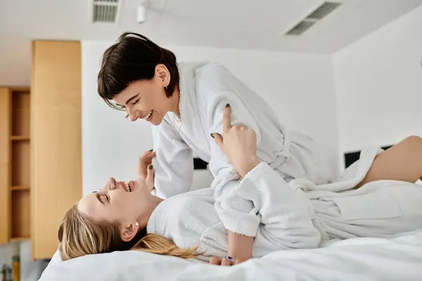 Um momento sereno capturado enquanto uma mulher se deita em uma cama ao lado de seu parceiro, ambos vestidos com roupões de banho dentro de um quarto de hotel. — Fotografia de Stock