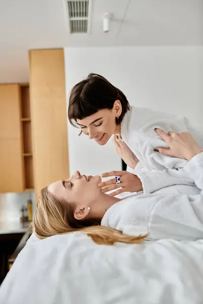A beautiful lesbian couple in bath robes, peacefully laying next to each other in a cozy hotel room. — Stock Photo