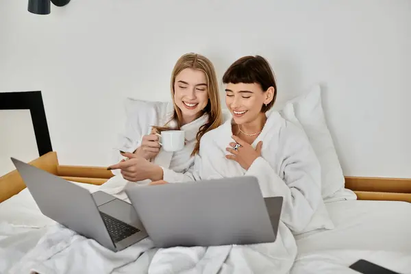 A beautiful lesbian couple in bath robes relax on a bed in a cozy hotel room. — Stock Photo