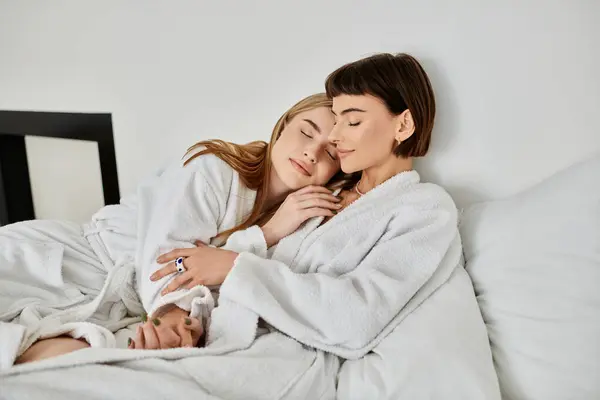 Ein schönes lesbisches Paar in Bademänteln kuschelt unter einer kuscheligen Decke auf einem Bett in einem Hotelzimmer. — Stockfoto