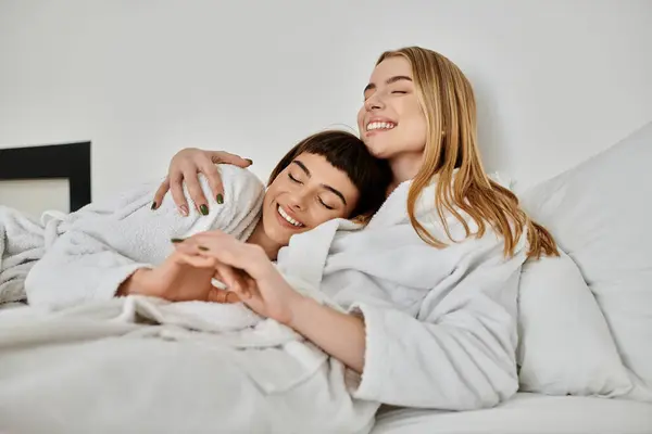 Un beau couple de lesbiennes en peignoirs de bain reposant paisiblement sur un lit confortable à l'intérieur d'une chambre d'hôtel. — Photo de stock