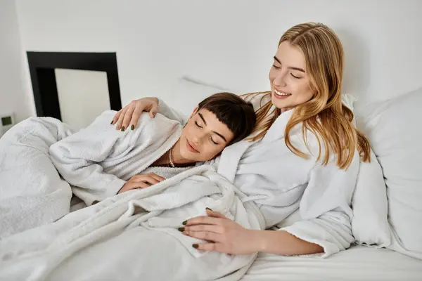 Zwei Frauen, ein schönes lesbisches Paar, in Bademänteln, liegen unter einer weichen Decke im Bett und teilen einen zärtlichen Moment. — Stockfoto