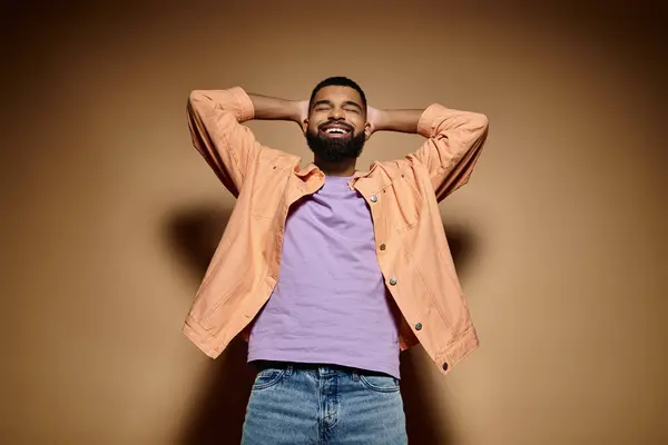 Elegante hombre afroamericano en traje de moda de pie con las manos en la cabeza delante de la pared vibrante. - foto de stock