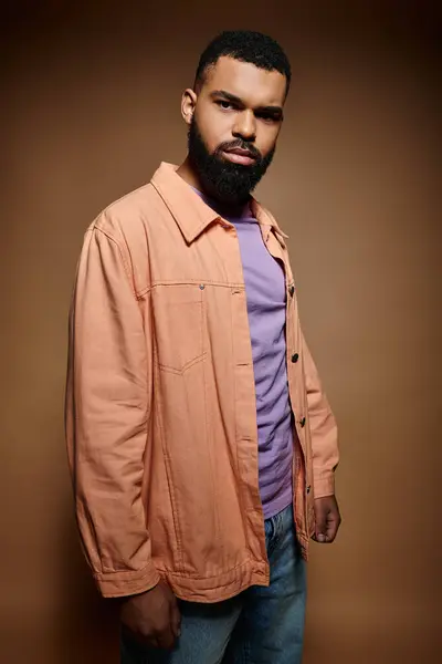 African American man in fashionable attire stands confidently before a rich brown background. — Stock Photo