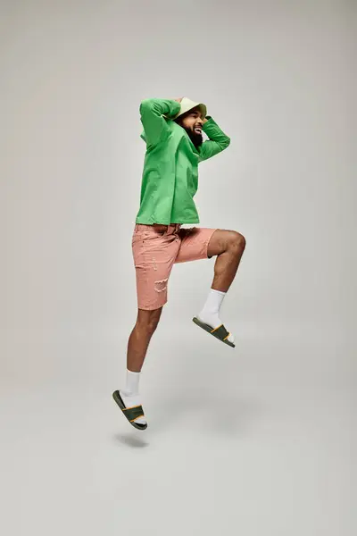 Bello afroamericano uomo colpisce una posa in giacca verde alla moda e pantaloncini rosa su uno sfondo vibrante. — Foto stock