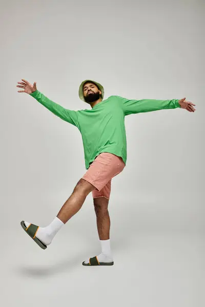 Handsome African American man poses in fashionable green shirt and pink shorts against vibrant backdrop. — Stock Photo