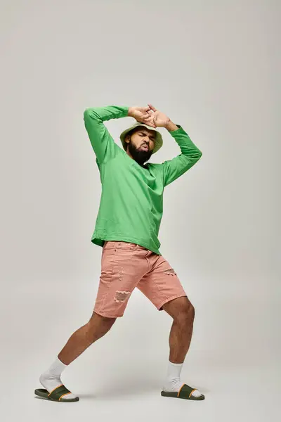 Handsome African American man posing in fashionable green shirt and pink shorts against vibrant backdrop. — Stock Photo