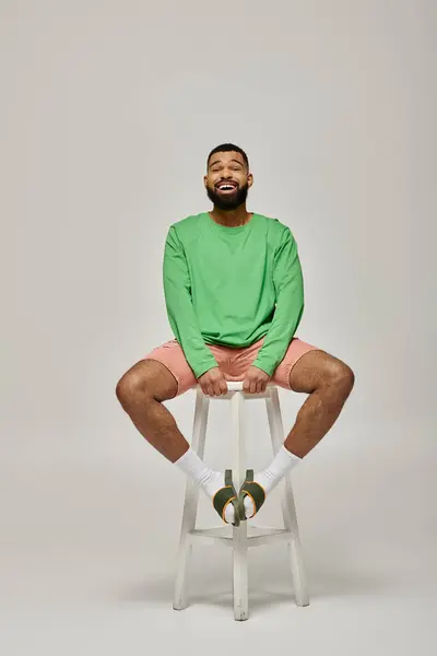 Hombre guapo en ropa de moda sentado en la parte superior de un taburete contra un fondo colorido. - foto de stock