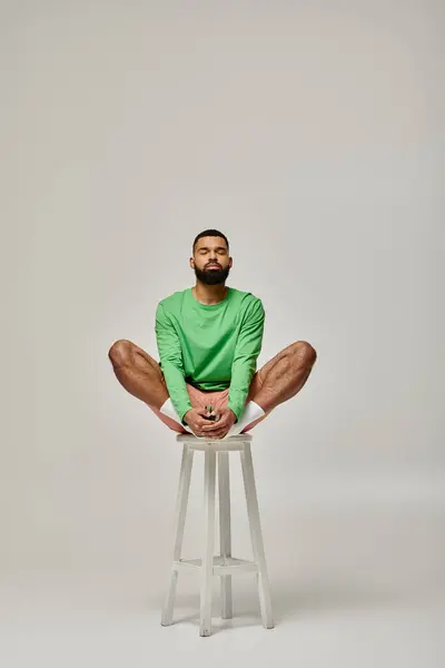 Handsome African American man sitting on a stool with his legs crossed. — Stock Photo