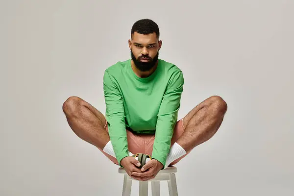 Handsome African American man in fashionable attire sitting on stool with legs crossed. — Stock Photo