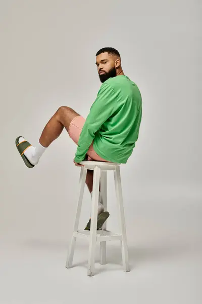 Handsome African American male striking a pose on a white stool against a colorful background. — Stock Photo