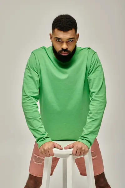 Handsome African American man in fashionable green shirt sitting on vibrant stool. — Stock Photo