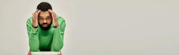 A man in casual attire sits with his head in his hands. — Stock Photo
