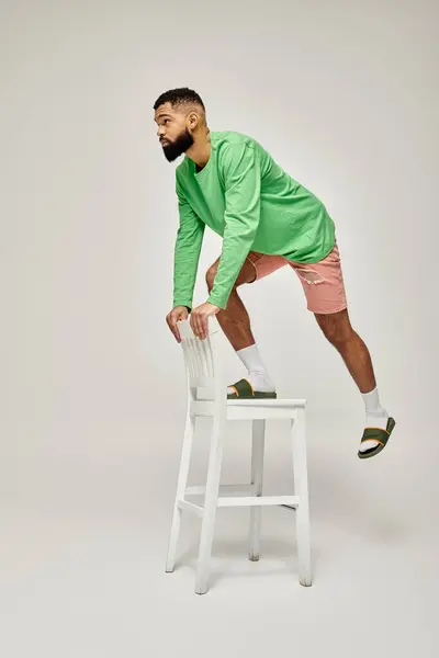 African American man in green shirt standing on stool against vibrant backdrop. — Stock Photo