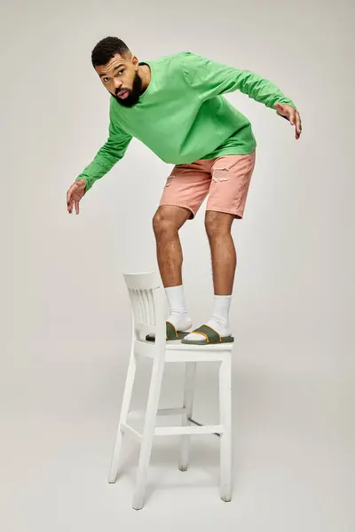 Stylish African American man stands on white chair against vibrant backdrop. — Stock Photo
