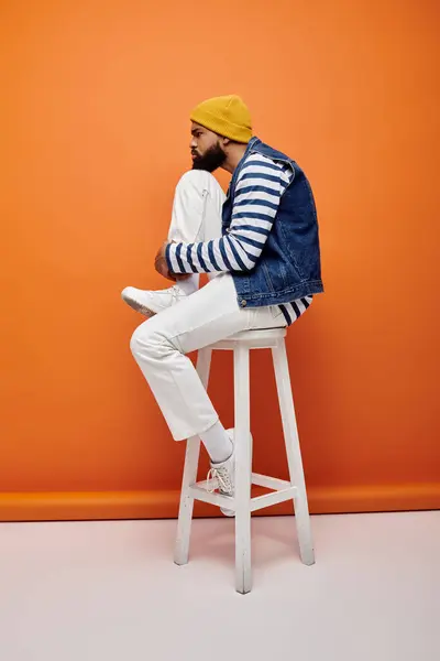 African American man in trendy outfit seated on white stool against colorful background. — Stock Photo