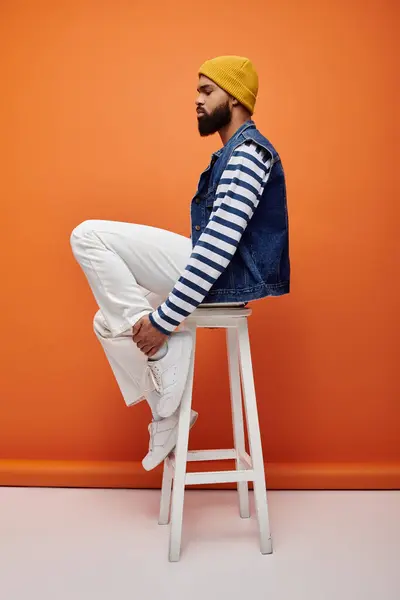 Handsome man in stylish outfit sitting gracefully on a vibrant stool. — Stock Photo