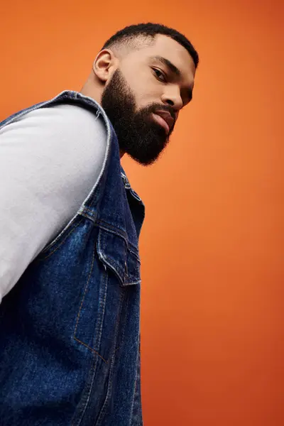 Handsome African American man with beard poses in denim vest on vibrant backdrop. — Stock Photo