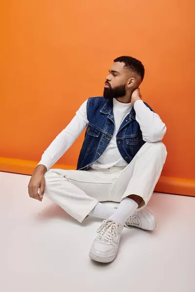 Handsome African American man sitting on vibrant backdrop in trendy outfit. — Stock Photo