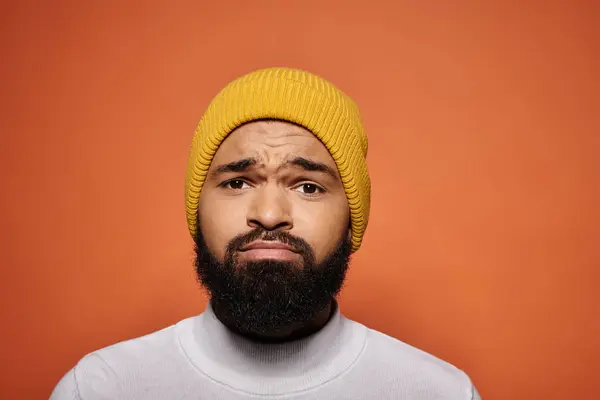 Elegante uomo afroamericano con la barba, con un cappello giallo, che colpisce una posa su uno sfondo vibrante. — Stock Photo