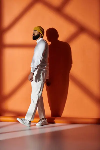 Handsome African American man in fashionable attire walking in front of vibrant orange backdrop. — Stock Photo