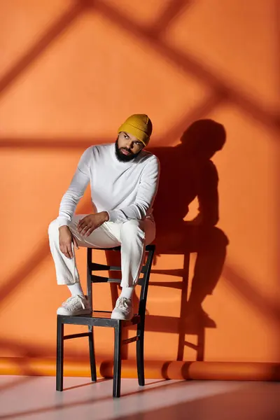 Schöner afroamerikanischer Mann in modischer Kleidung sitzt auf einem Holzstuhl vor einer lebendigen Kulisse. — Stockfoto